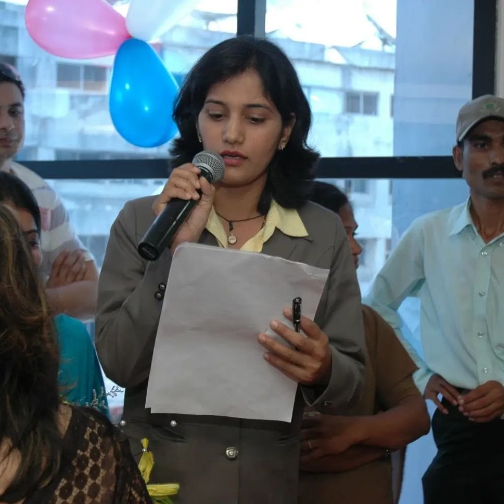 Portrait of Anjali Wadje, a professional middle-aged Indian woman in formal attire, smiling confidently with a neutral dark background